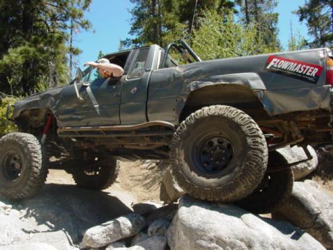 1986 Ford Bronco - Modified pickup truck with large tires navigating rocks on an off-road trail.