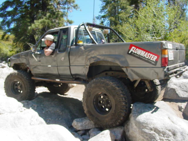 gray pickup truck with big tires crawling over rocks on a trail
