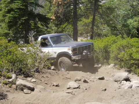 1986 Ford Bronco - Ford Bronco tackles a challenging off-road path through trees and rocks.