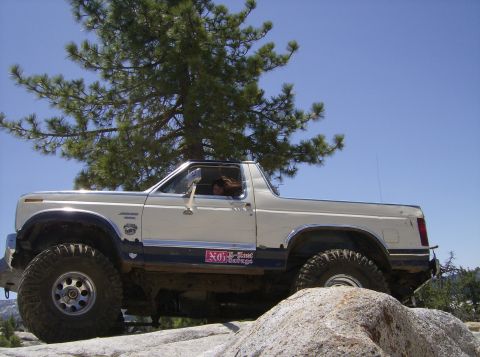 1986 Ford Bronco - A white Ford Bronco navigates a rocky trail with large off-road tires.