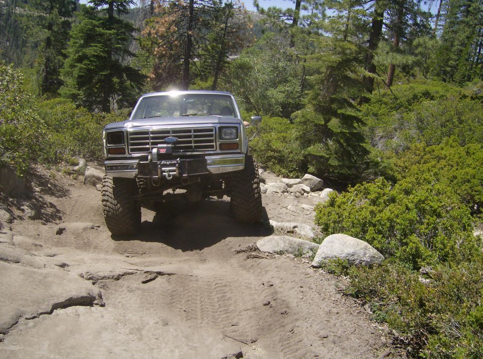 Modified 1980s Ford Bronco with large tires on a rocky off-road trail