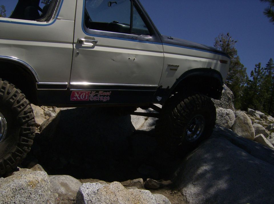 1986 Ford Bronco 3q-front view, white and black, off-roading on rocks with large tires