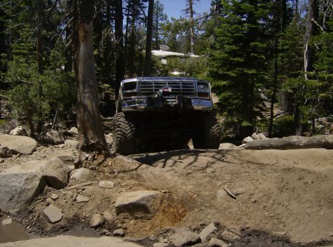 1986 Ford Bronco - A lifted Ford Bronco navigates a challenging off-road path through a forest.