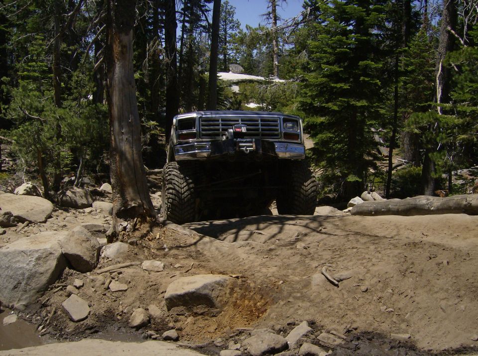 Front view of a lifted, modified Ford Bronco on a rocky, wooded trail. Chrome grille, winch visible