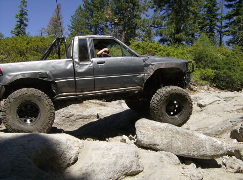 1986 Ford Bronco - This heavily modified pickup truck is shown tackling a challenging rocky trail with its large off-road tires.