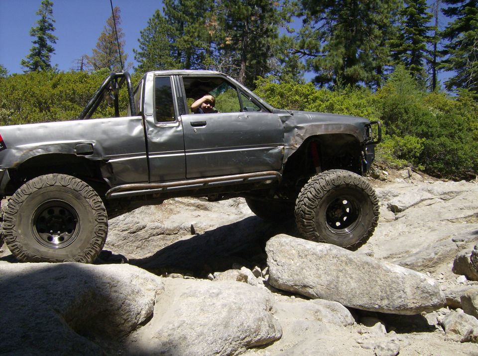 Gray off-road pickup truck with roll cage navigating rocky terrain