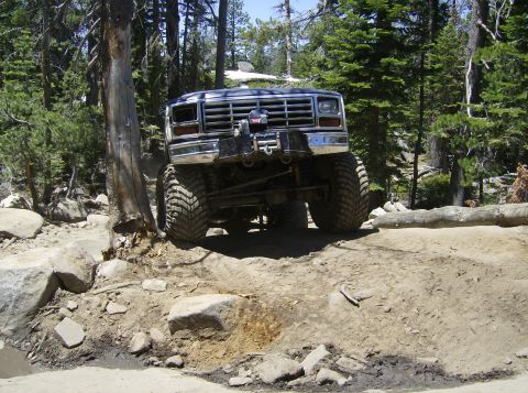 1986 Ford Bronco - Modified Ford Bronco navigates a challenging rocky off-road trail in a wooded area.