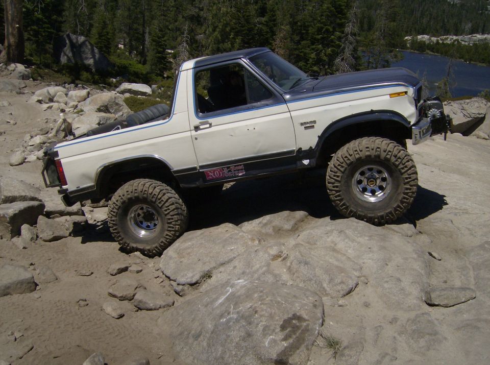 White and gray Ford Bronco off-roading on rocks, with a spare tire in the bed