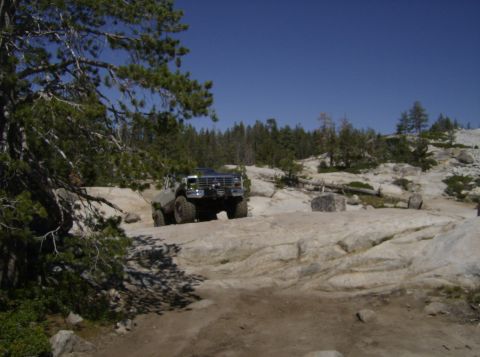1986 Ford Bronco - An off-road SUV navigates a challenging rocky path under a clear blue sky.