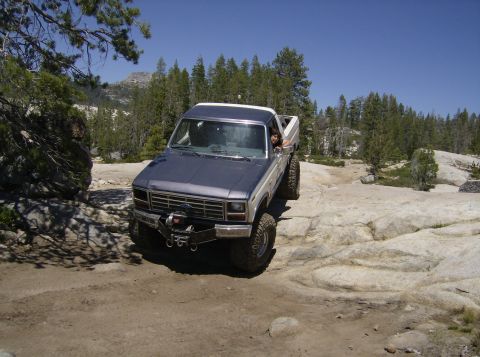 1986 Ford Bronco - Ford F-Series truck navigates a rocky trail under a clear blue sky.