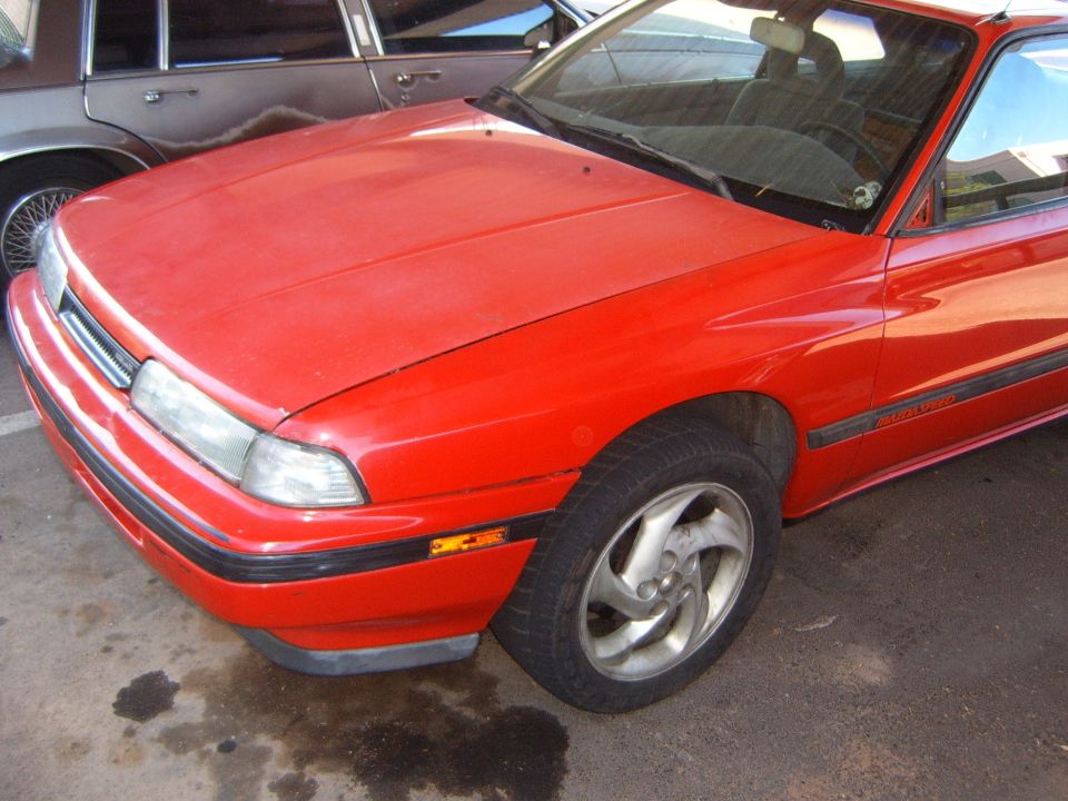 Faded red Mazda MX-6 coupe front 3/4 view on asphalt with alloy wheel and black trim