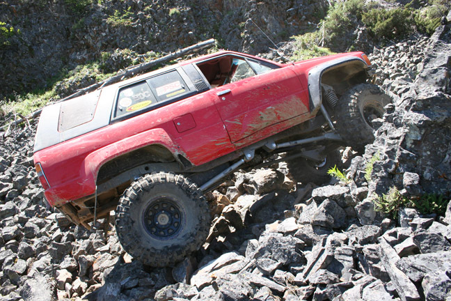 Red SUV with off-road modifications climbing a rocky incline