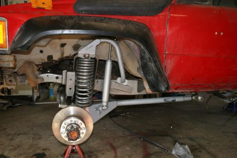 1993 Ford Bronco - Close-up of a red SUV's front suspension system, a lifted coilover and shock absorber assembly.