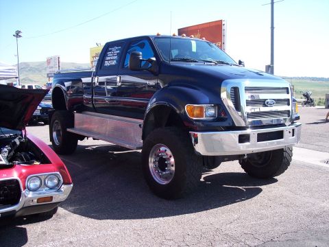1972 Ford Ranchero - A dark blue Ford F-650 truck is parked next to a red classic car at an outdoor event.