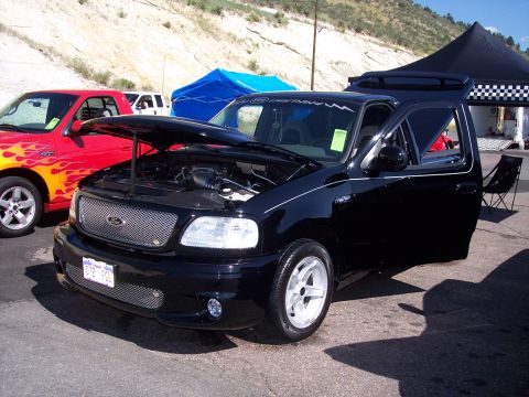 1972 Ford Ranchero - Black 1999 Ford F-150 Lightning pickup truck with hood open at an outdoor event.