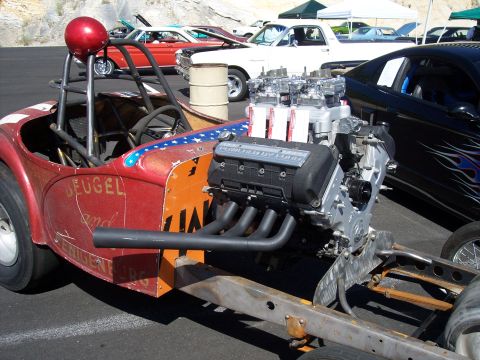 1972 Ford Ranchero - A custom-built dragster is displayed with its powerful engine prominently visible, alongside other vehicles in the background.
