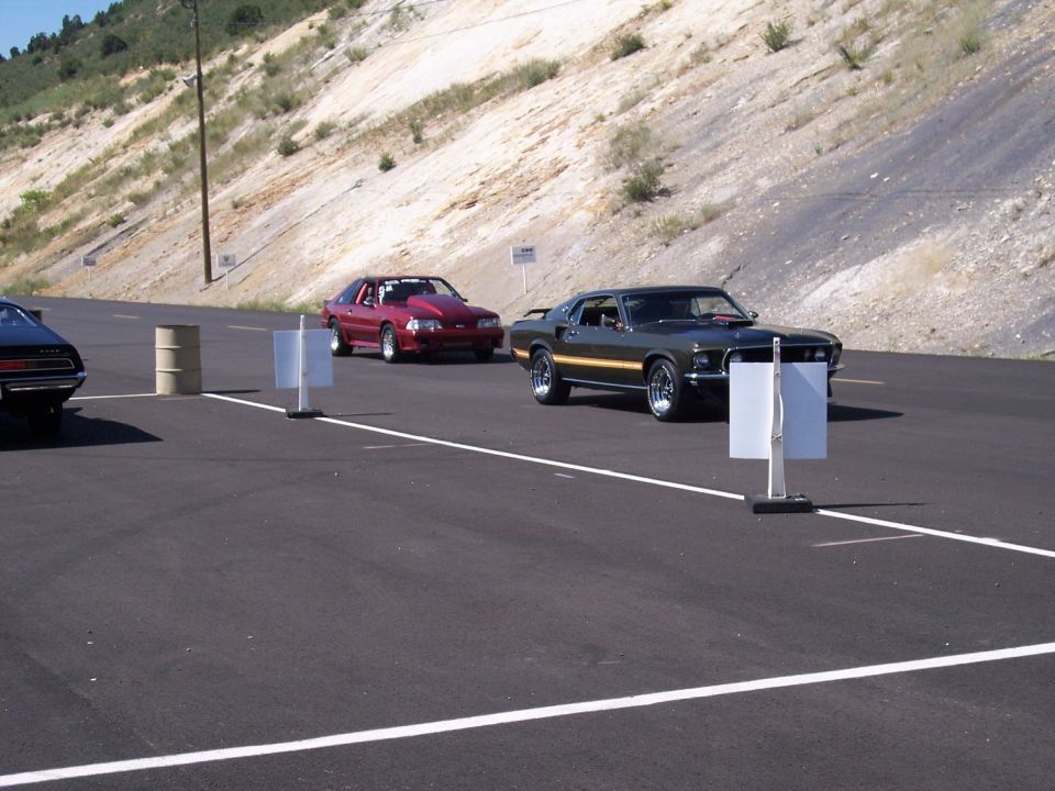 Dark green 1969 Ford Mustang Mach 1 and a red Ford Mustang in a staging lane
