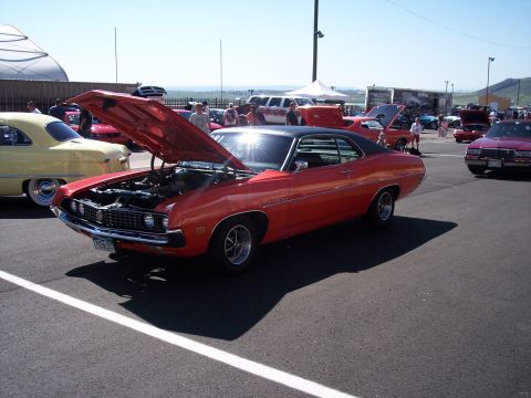 1972 Ford Ranchero - A red coupe with its hood open, parked at an outdoor car show. Other vehicles and spectators are visible in the background.