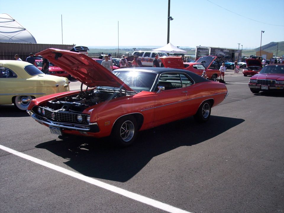 Orange Ford Torino fastback with hood raised at an outdoor car show