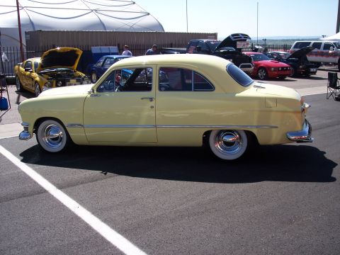 1972 Ford Ranchero - A classic yellow Ford sedan with whitewall tires is displayed at a car show with other vehicles present.