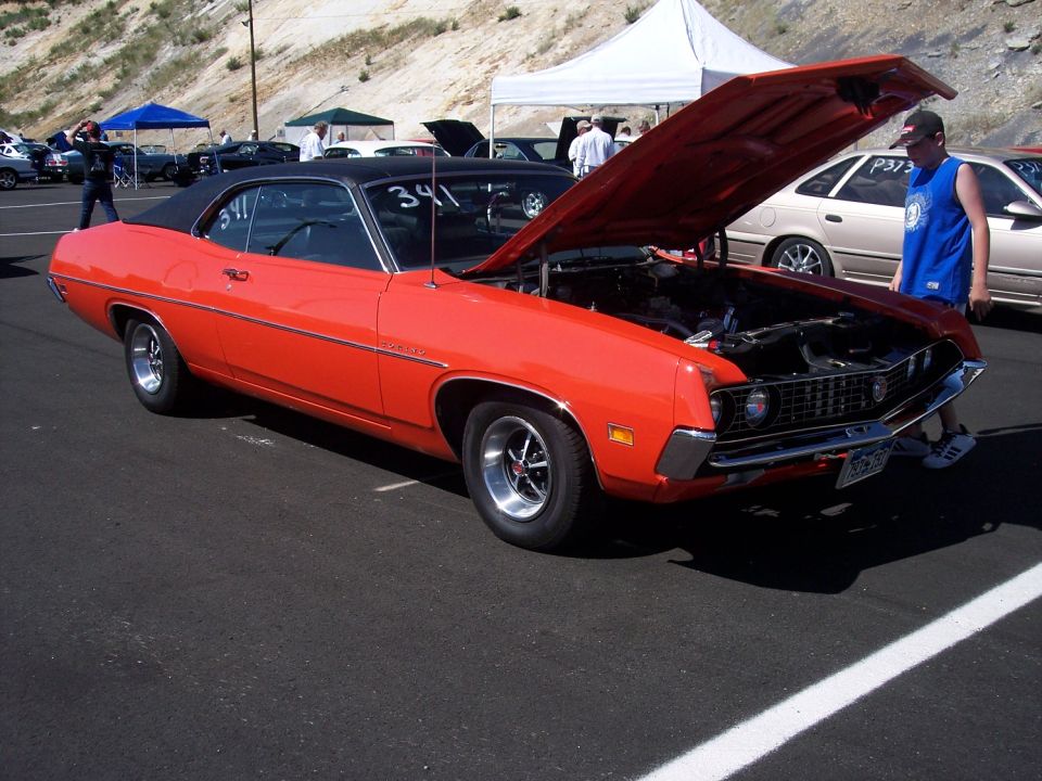 Orange 1970 Ford Ranchero with black top, hood open, parked on asphalt