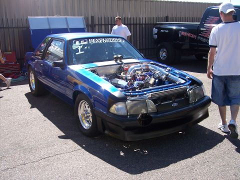 1972 Ford Ranchero - Modified blue Ford Mustang at Bandimere Speedway, engine exposed, with a black pickup truck in the background.