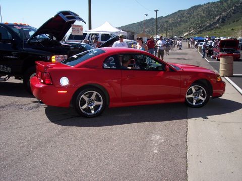 1972 Ford Ranchero - A red coupe is parked next to a black truck at an outdoor event with spectators in the background.