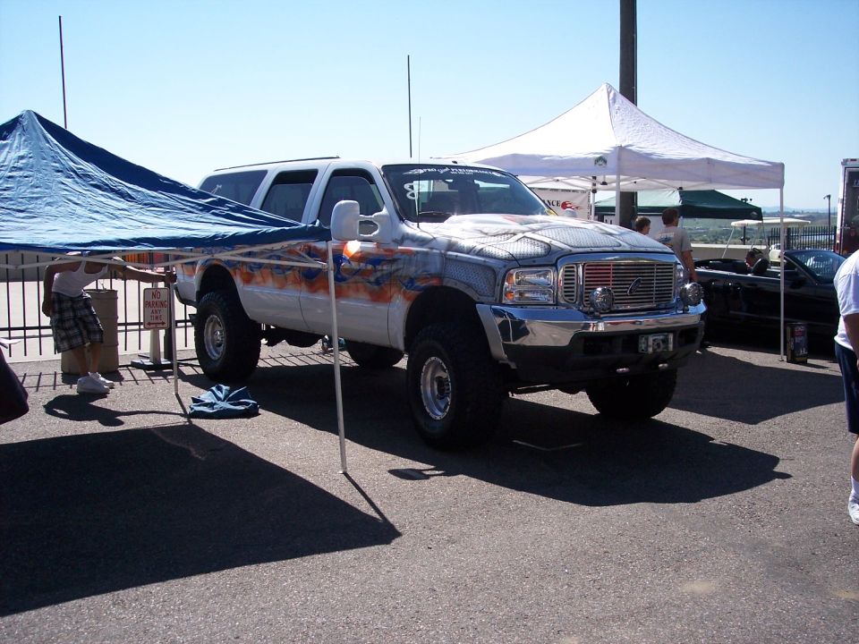 Lifted white SUV with flame graphics and custom grille. Another car is parked behind it