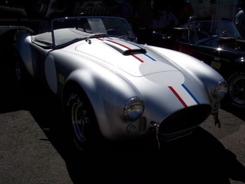 1972 Ford Ranchero - A silver AC Cobra replica with racing stripes is parked next to another car.
