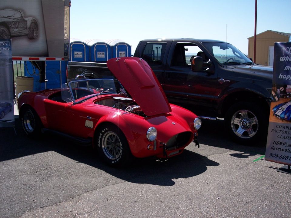 Red convertible sports car with hood open parked next to a dark pickup truck