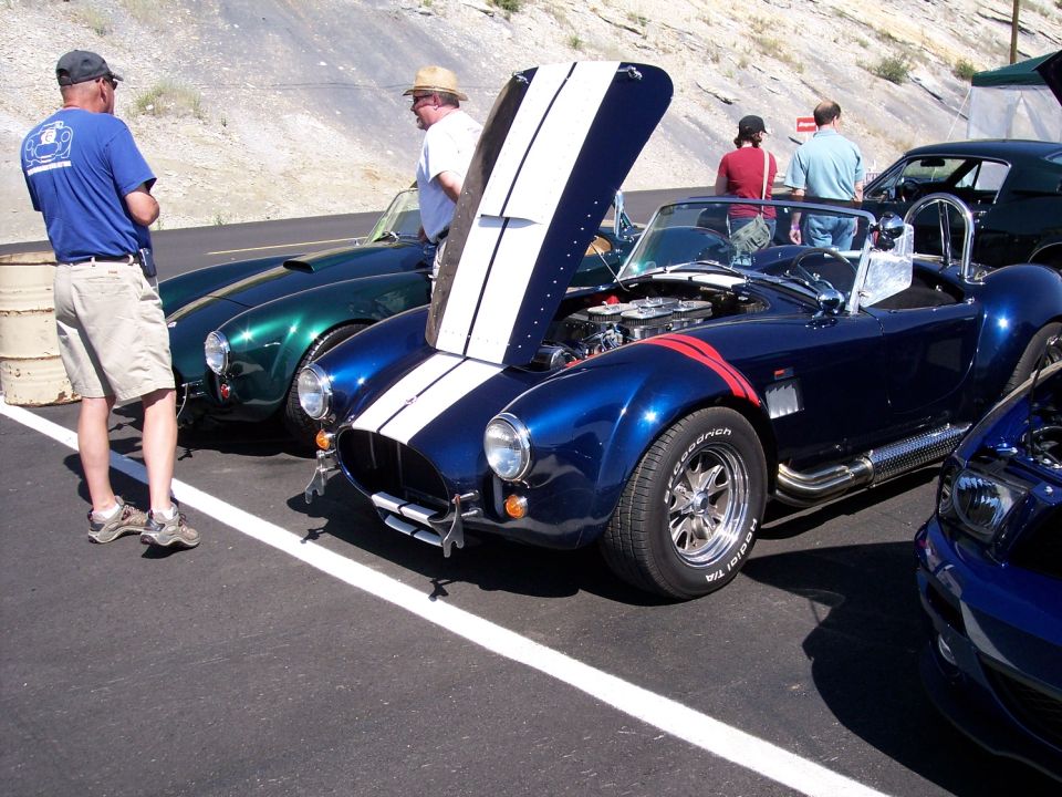 Blue convertible with white racing stripes and hood open, parked next to a green convertible