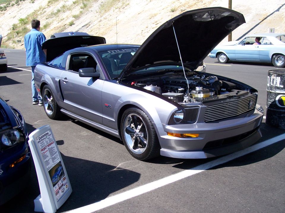 Silver 2005 Ford Mustang GT coupe, front 3/4 view, hood open, chrome wheels, parked on asphalt
