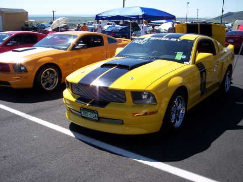 1972 Ford Ranchero - A yellow Shelby Mustang with black racing stripes is parked at an event, with another orange Mustang nearby.