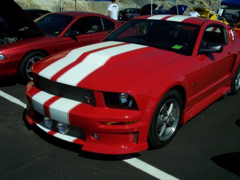 1972 Ford Ranchero - A red 2005 Ford Mustang GT with white racing stripes is parked at an outdoor car show.