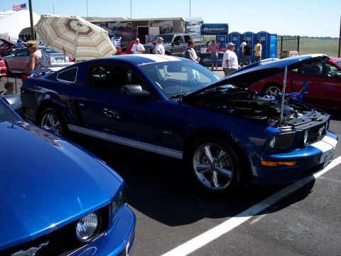 1972 Ford Ranchero - A blue Ford Mustang GT with white racing stripes is parked at an outdoor event with its hood open.