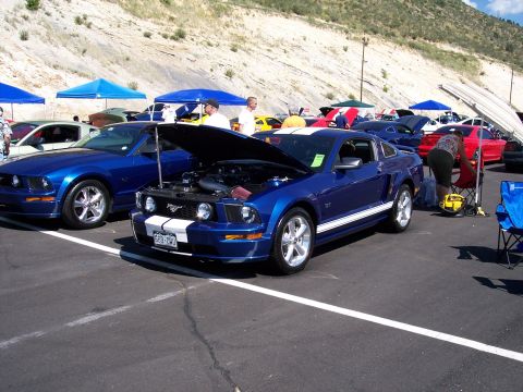 1972 Ford Ranchero - Two blue Ford Mustangs are displayed at an outdoor car show with a rocky hillside in the background.