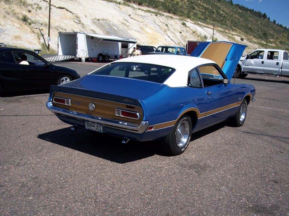Blue Ford Maverick Grabber with white roof and gold stripe, hood open. Black car and white truck nearby