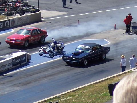 1972 Ford Ranchero - A dark blue coupe with a hood scoop is on the drag strip, kicking up smoke.