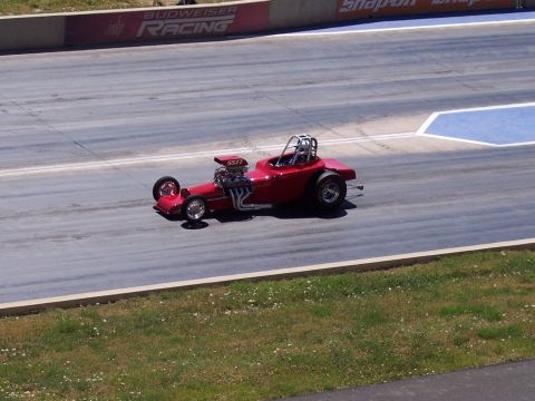 1972 Ford Ranchero - A red dragster with a prominent engine and roll cage is on a drag strip.