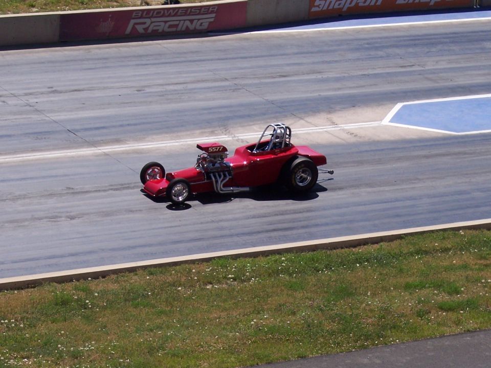 Red dragster with roll cage and exposed engine on a drag strip, number 5577 visible