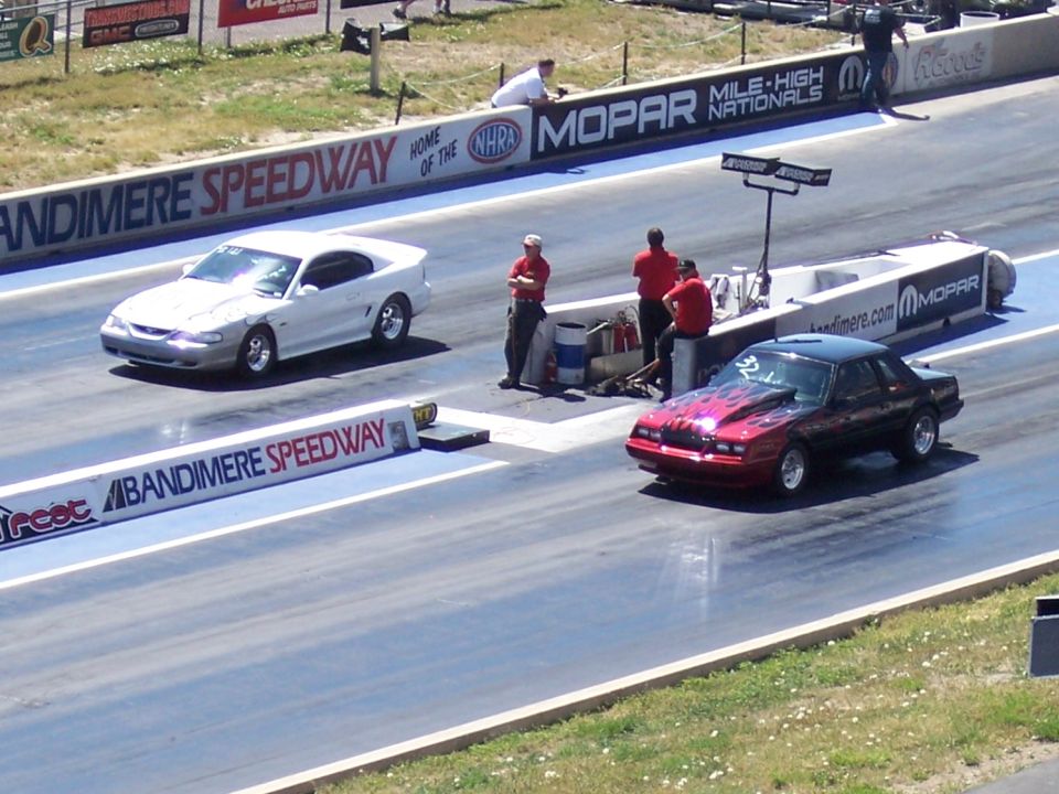 Red and black drag car with flame graphics on the hood, at a drag strip