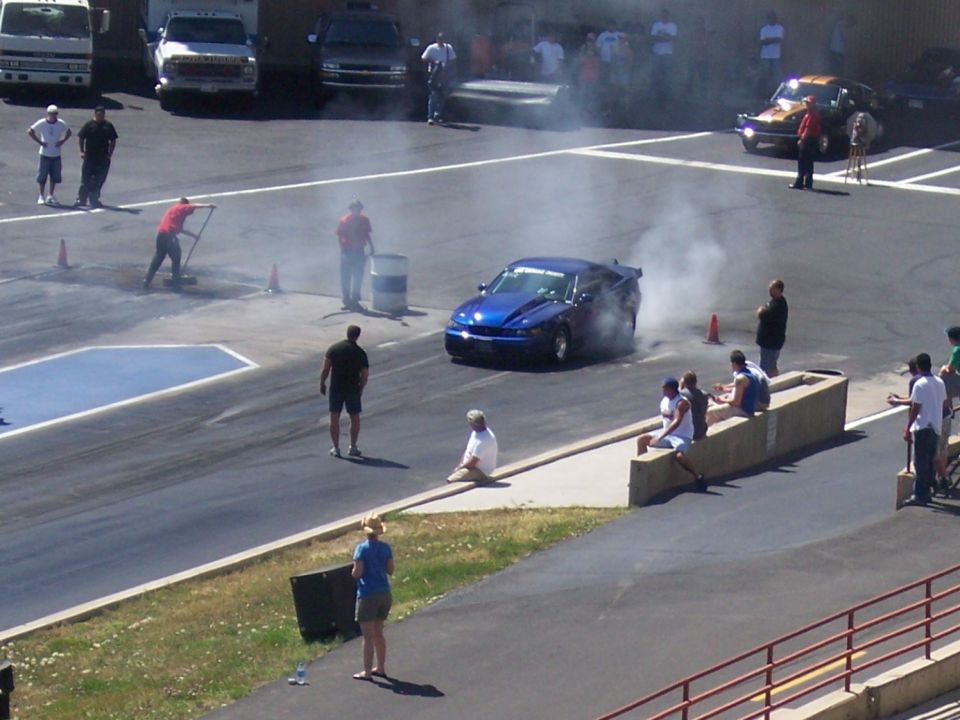 Blue muscle car doing a burnout on a drag strip, with spectators watching