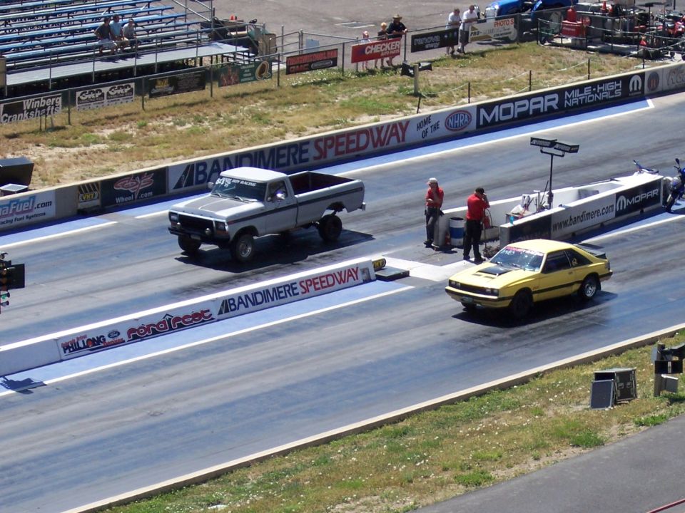 Yellow coupe drag racing on a track, front 3/4 view