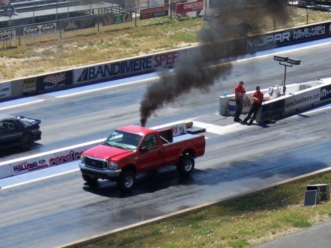 1972 Ford Ranchero - A red pickup truck races down a drag strip, leaving a trail of black smoke.