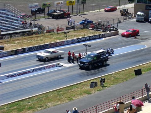 1972 Ford Ranchero - Two vehicles race down the drag strip at Bandimere Speedway, with spectators watching.