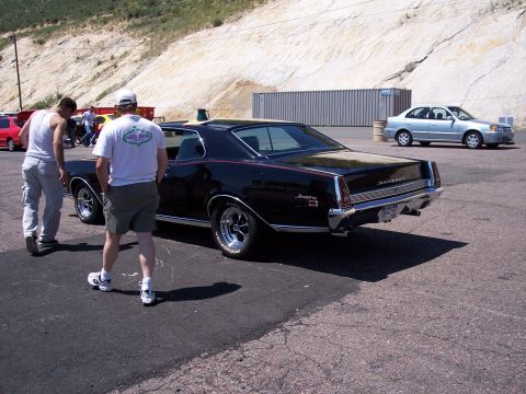 1972 Ford Ranchero - A black coupe with chrome accents and a red stripe is parked outdoors, with two men walking away from it.