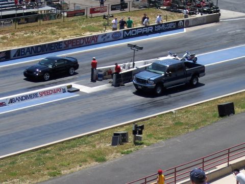 1972 Ford Ranchero - Two vehicles race down the drag strip at Bandimere Speedway, with spectators in the background.