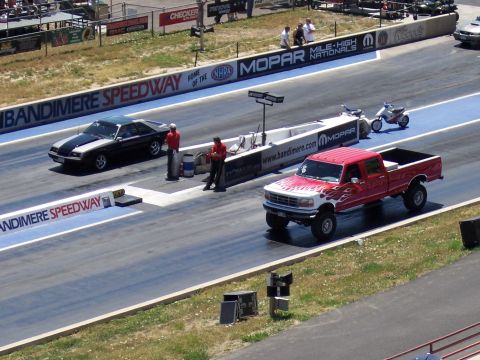 1972 Ford Ranchero - Two vehicles on a drag strip at Bandimere Speedway, with spectators in the background.