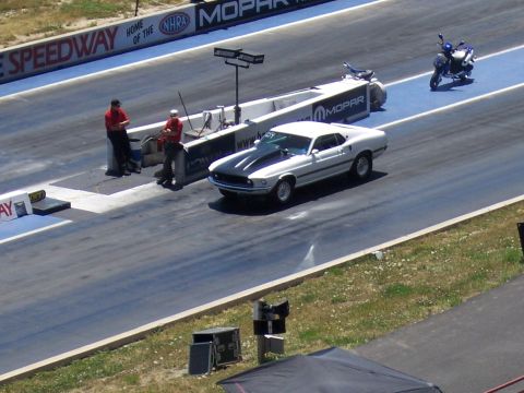 1972 Ford Ranchero - A white muscle car with black racing stripes is staged on a drag strip, with a motorcycle visible in the background.