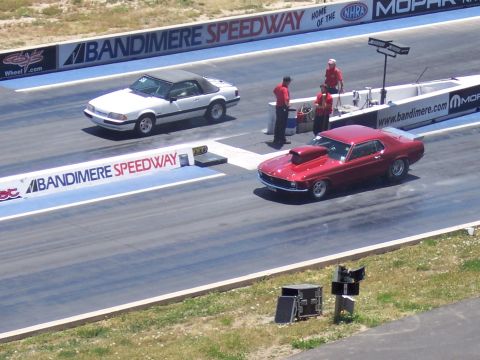 1972 Ford Ranchero - Two cars prepare for a drag race at Bandimere Speedway, with a red muscle car in the foreground and a white convertible behind it the backg…